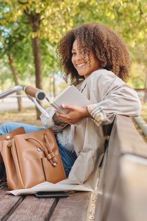 Smiling Black Latina woman with book on bench