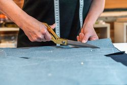 Seamstress using scissors to cut textile at work table.