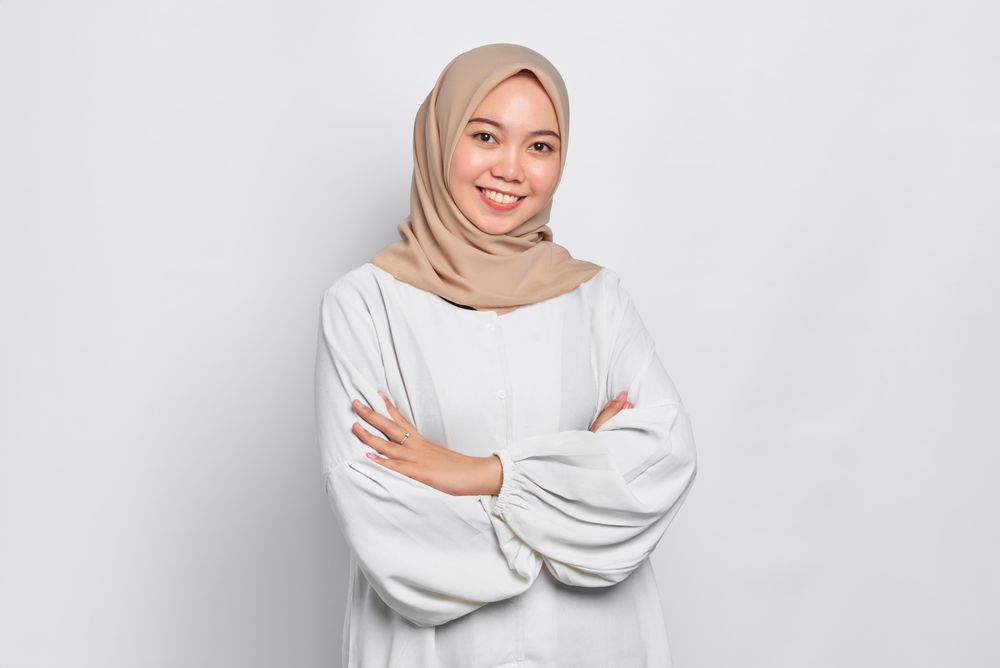Happy Asian female in headscarf with arms crossed and looking at camera