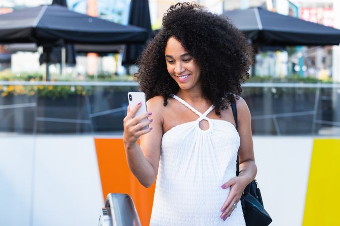 Pregnant Black woman browsing smartphone on escalator