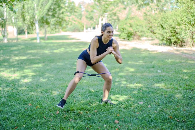 In the park, a woman exercises outdoors using a resistance band, focusing on health and fitness activities