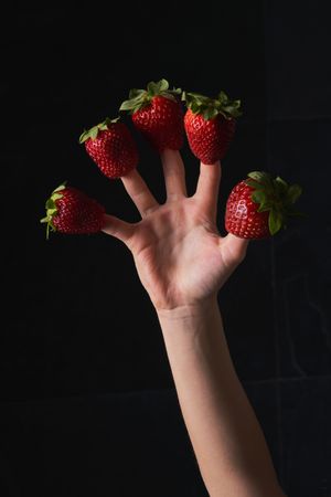Hand of of faceless person showing fresh strawberries on fingers