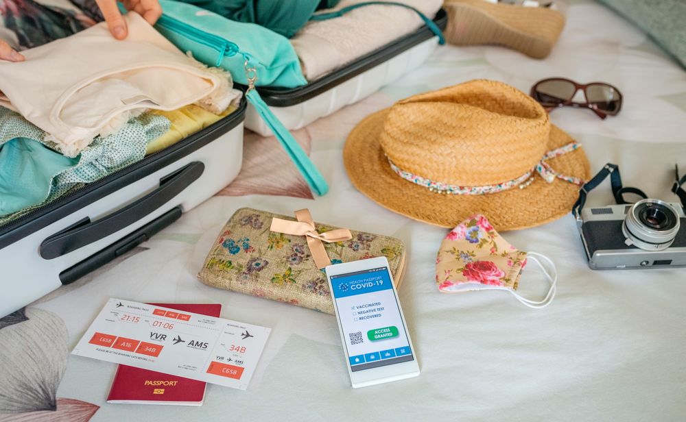 Woman preparing suitcase for vacation and mobile phone with covid green pass