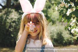 Close up of a smiling girl holding a painted easter egg in front of her face 4Mqg14