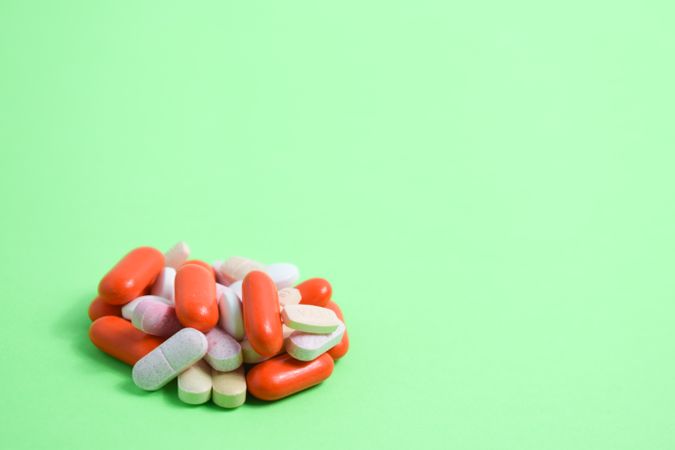 Pile of colorful medication and vitamins on green table with copy space