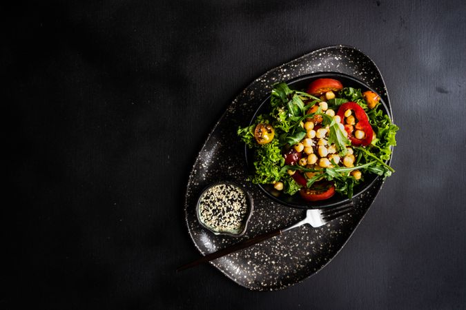 Top view of organic vegetable salad with garbanzo beans and sesame seeds on dark counter with copy space