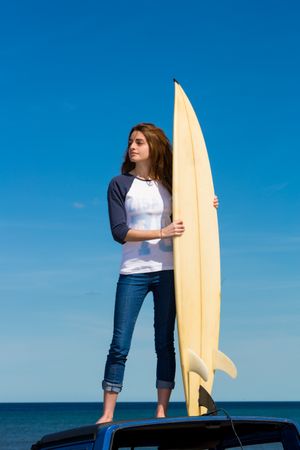 Woman with surfboard standing on roof of car