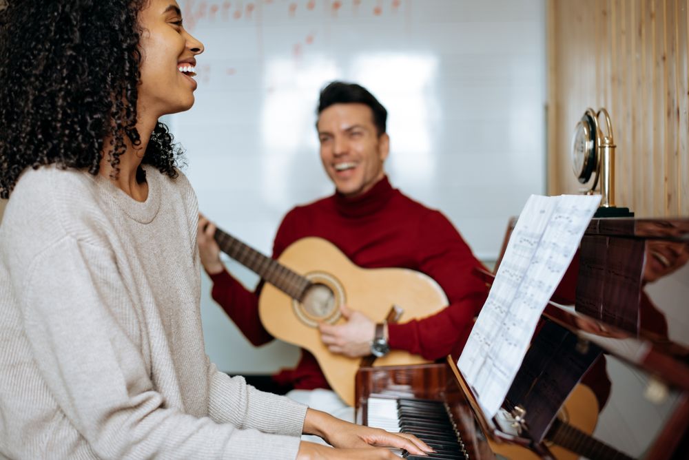 Woman playing piano near man playing guitar in studio
