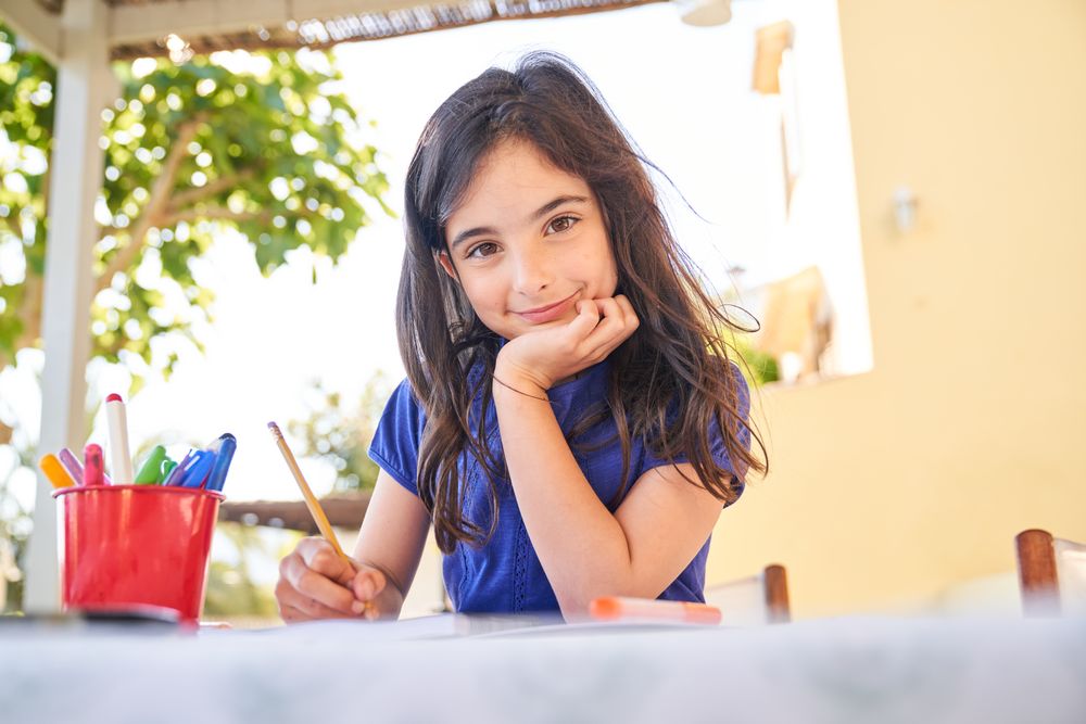 Charming girl sitting at table and drawing picture