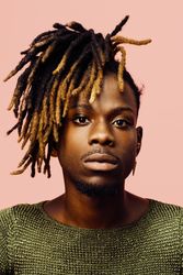 Portrait of a serious young man in green with dreadlocks and red sunglasses, isolated on pink