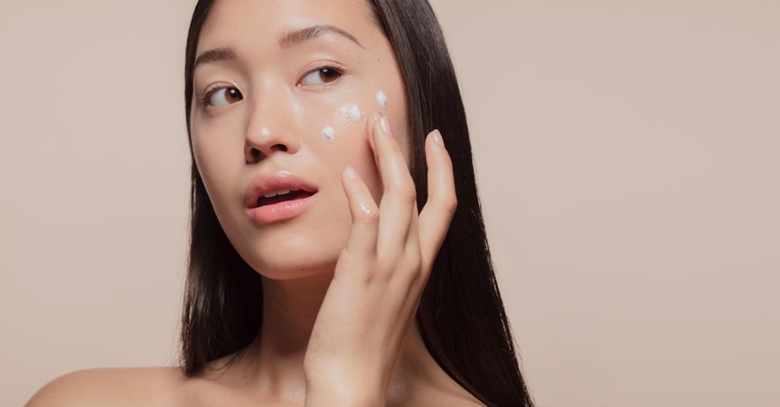 Close up of a youthful female model applying moisturizer to her face