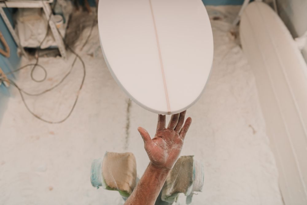 Man in respirator polishing surf board in workshop