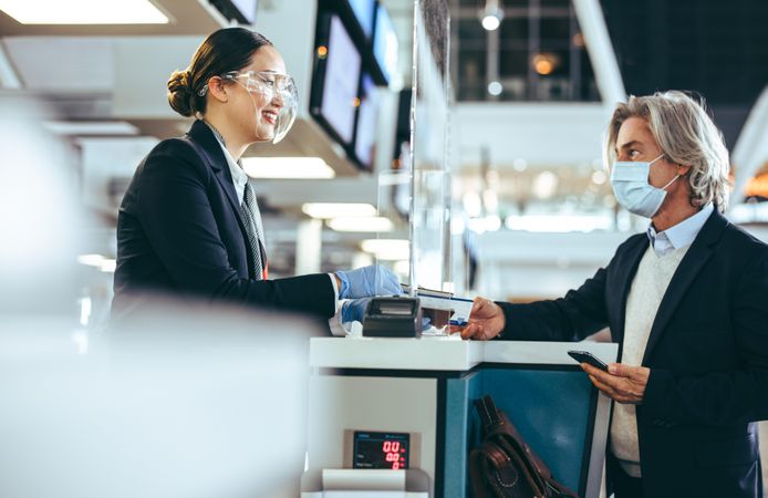 Airline attendant wearing protective face shield assisting passenger at check in counter
