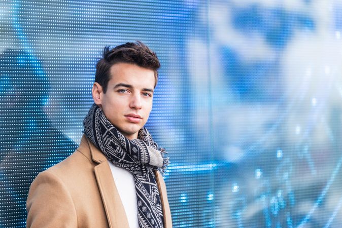 Portrait of handsome young man in fall coat against digital wall looking at camera