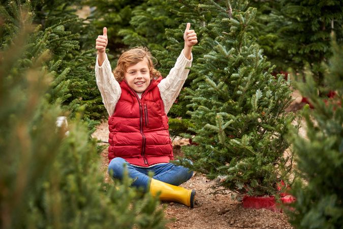 Cheerful child with thumbs up in Xmas trees