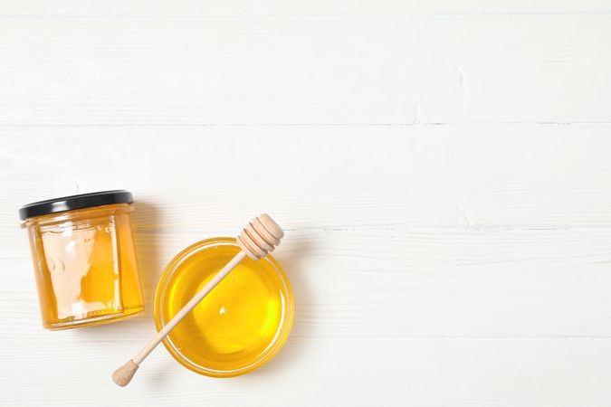 Glass jar and bowl with honey, dipper on wooden background, space for text