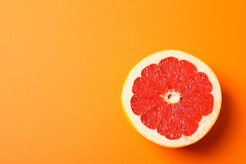 Grapefruit slice on orange background, space for text