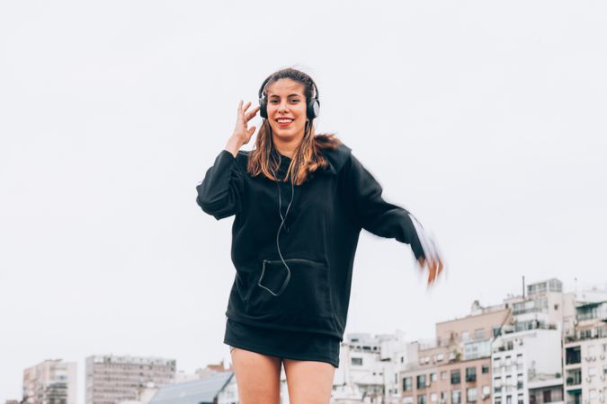 Content young woman in casual wear dancing while using headphones at city street