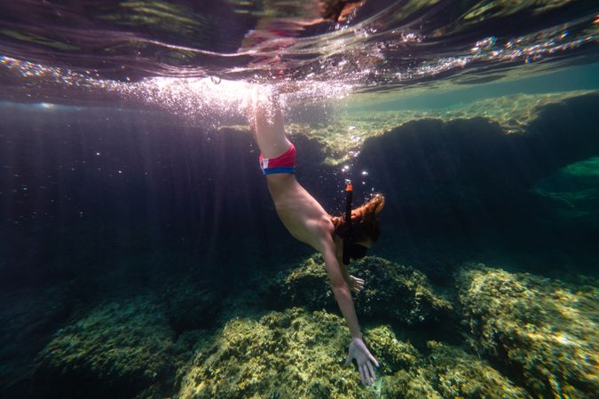 Teen boy diving in sea water on bottom with reef