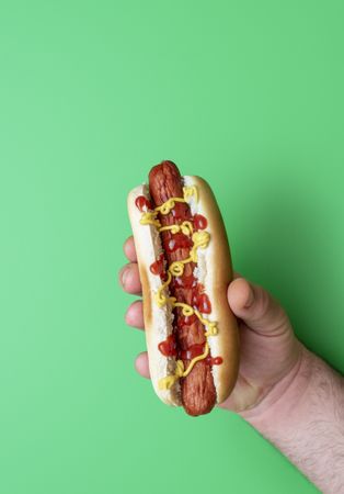 Male hand holding hot dog over green background