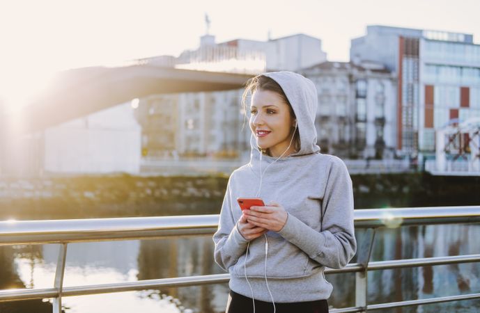 Woman with earphones wearing a hoodie on a embankment