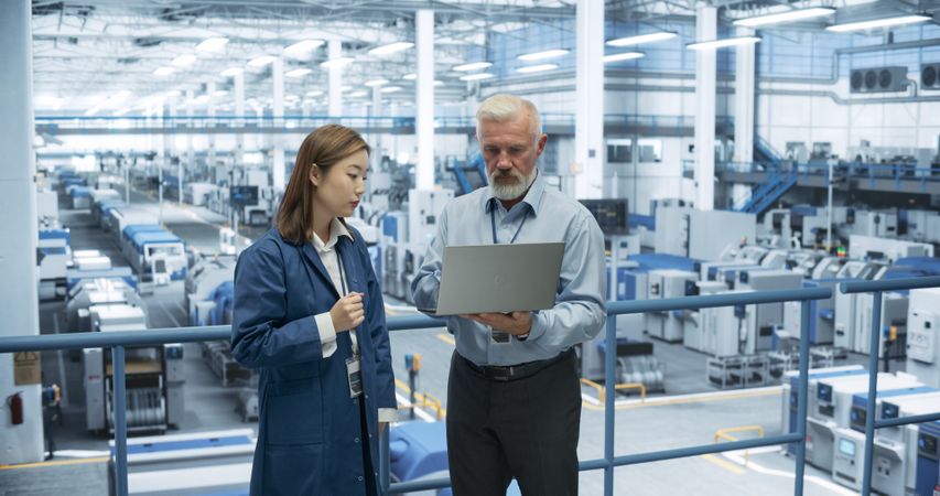 Industrial Engineers Working at a Technology Factory. Man and Japanese Female Using Laptop Computer and Having a Conversation. Portrait of a Couple at Work