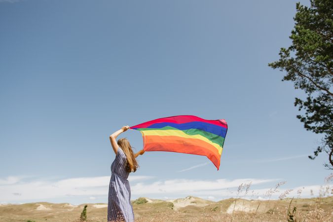 Young woman with rainbow banner against sky