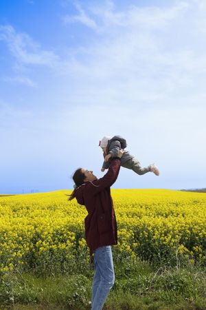 Woman throwing her baby in the air in front of yellow field