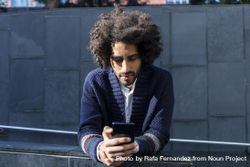 Black man in cardigan leaning forward outdoors on sunny day using cell phone 5qkP6Y