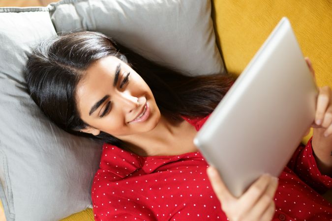 Woman relaxing on sofa while reading a tablet