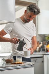 Serious man pouring coffee from moka pot in kitchen