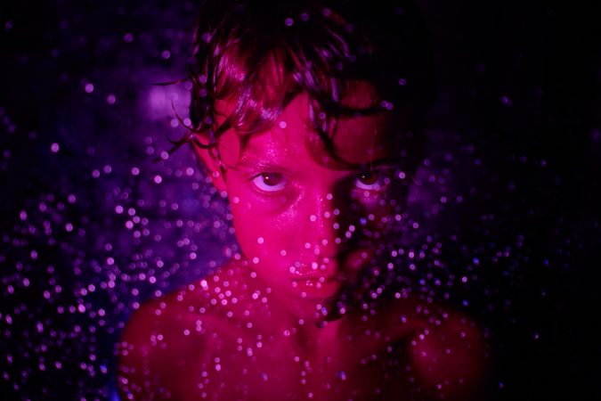 Displeased boy with wet hair in neon light