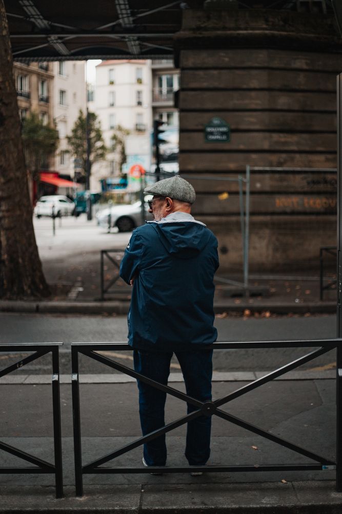 Back view of older man standing on sidewalk near fence