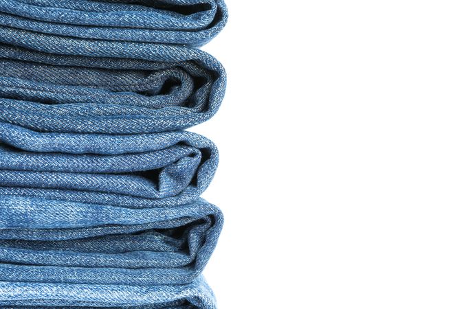 Stack of blue jeans on light background, space for text