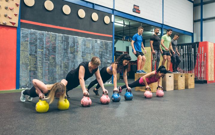 Sportswomen training with kettlebells and sportsmen doing box jumps