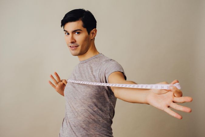 Hispanic male holding measuring tape out in front of him in beige studio shoot