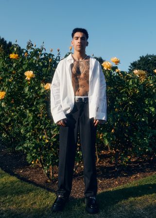 Man with open shirt standing in front of yellow flowers