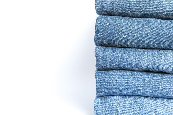 Stack of blue jeans on light background, space for text