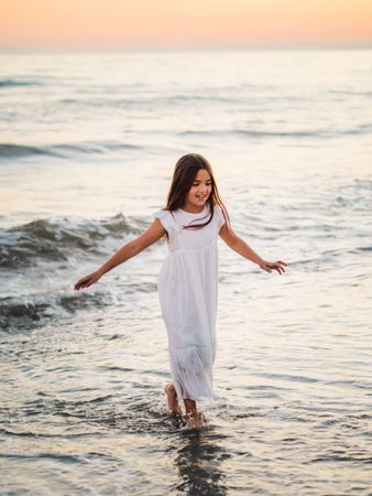 Adorable girl walking and playing on seaside at sunset