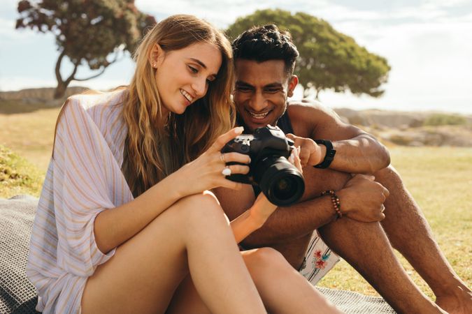 Smiling man and woman sitting in a park checking photos on view screen of dslr camera