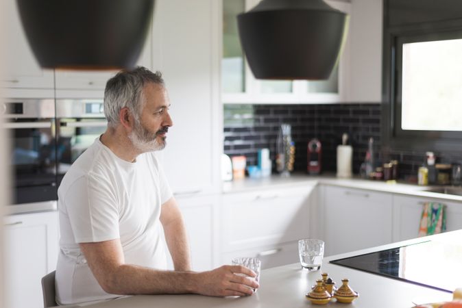 Bearded man sitting in the kitchen holding a glass of water