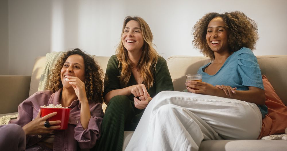 Portrait of Happy Group of Female Friends Watching a Funny Show and Laughing in Cozy Living Room.