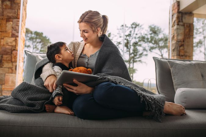 Mother and son wrapped in blanket relaxing in living room