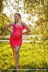 Pregnant female in pink dress standing under trees on the grass on sunny day 5rRMP5
