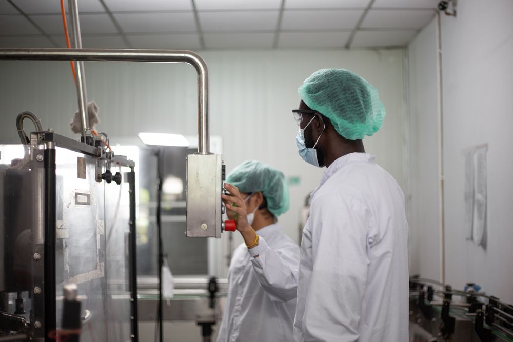 Two diverse factory workers are inspecting machinery inside a beverage production facility.