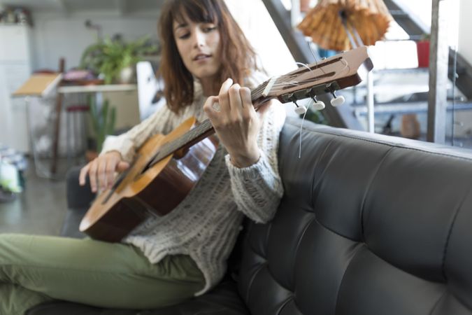 Female on sofa playing acoustic guitar in her living room