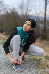 Young woman looking away while tying her shoe laces