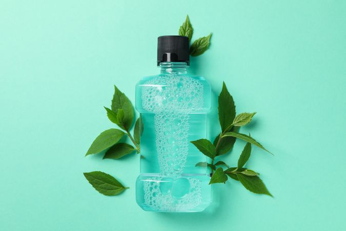 Mouthwash and leaves on mint background, space for text