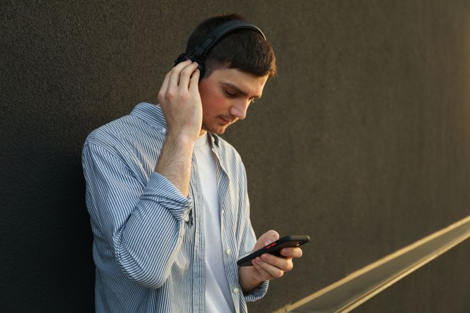 Young man in headphones listen music against wall