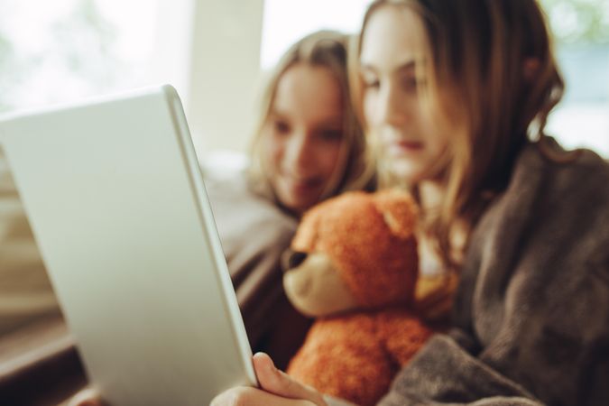Two girls covered in warm blanket watching a movie on a tablet pc at home